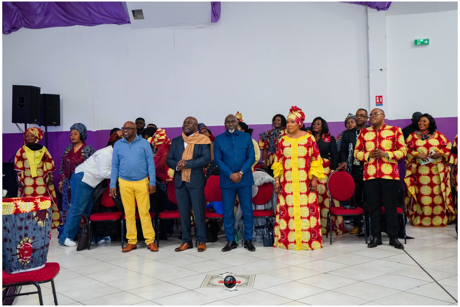 Group of people in colorful traditional outfits standing on a stage indoors at an event.