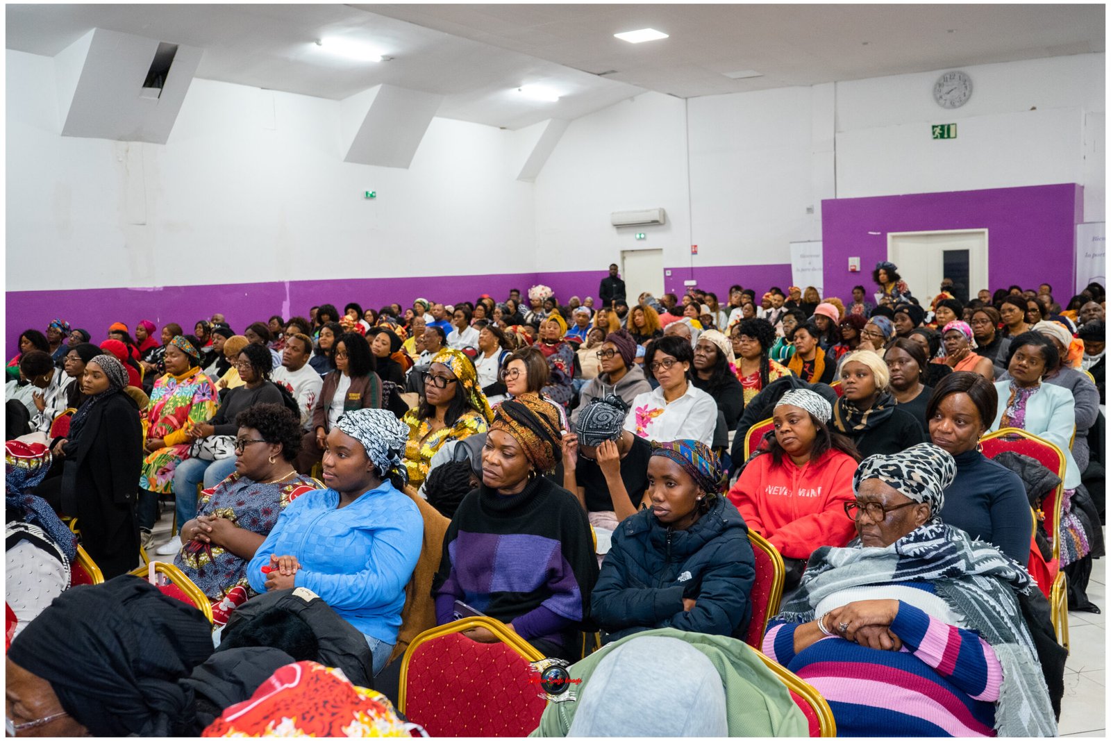 Large group of people seated in a hall with purple walls, attending an event or gathering.
